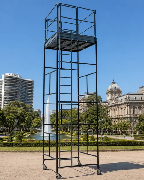 torre de andaime tubular preta montada num jardim, com prédios ao fundo