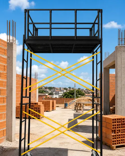 torre de andaime industrial preta com rodízios, guarda-corpo e travamento amarelo, numa obra